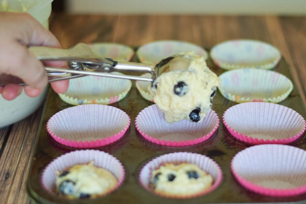 scooping the muffin batter into paper lined muffin pan