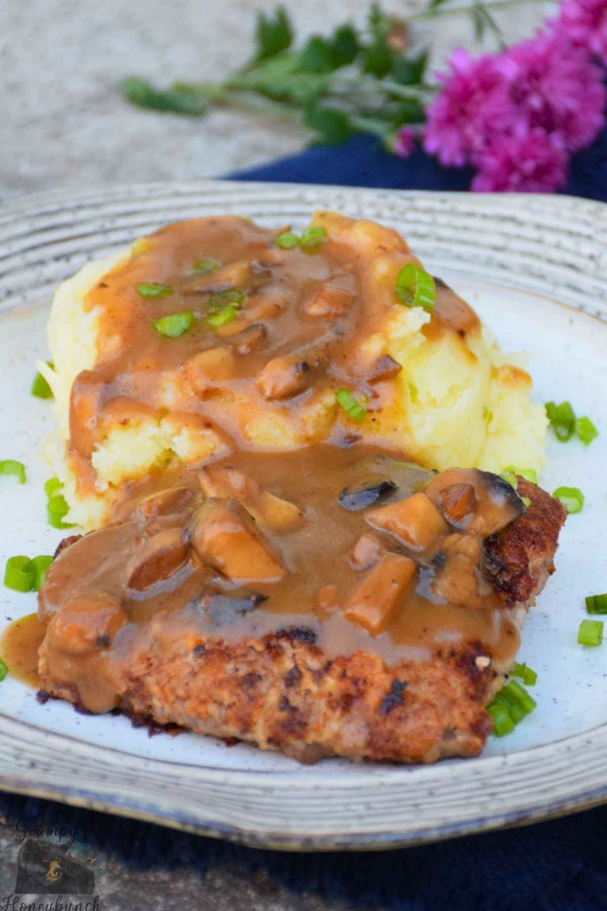A plate with country fried steak topped with mushroom gravy with a side of mashed potatoes and gravy.