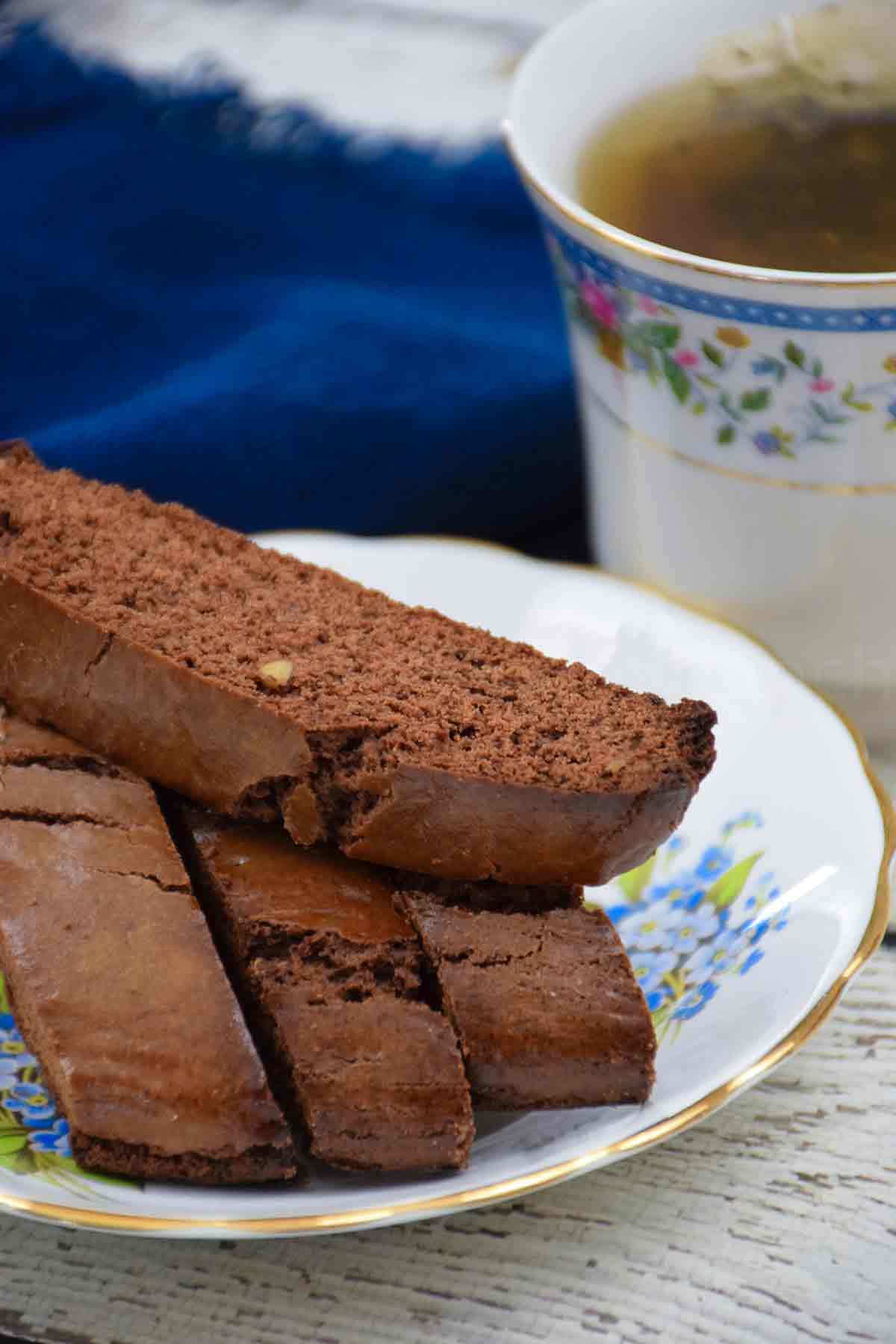Brownie Biscotti stacked on a plate with a cup of tea in the background.