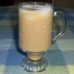 A clear crystal glass with iced coffee and pieces of ice floating on the top.