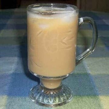 A clear crystal glass with iced coffee and pieces of ice floating on the top.