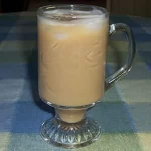 A clear crystal glass with iced coffee and pieces of ice floating on the top.