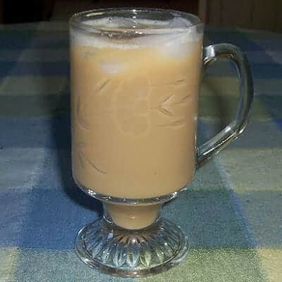 A clear crystal glass with iced coffee and pieces of ice floating on the top.