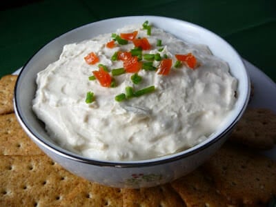 Clam Dip in a white bowl with red pimento and green chive top garnish