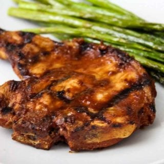 Up close image of grilled pork chop with chipotle sauce on a white plate with side of asparagus