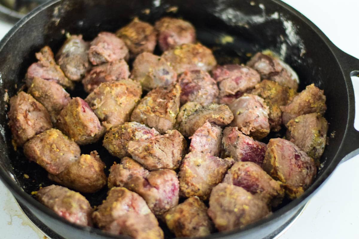 Venison meat being browned in skillet with flour coating.