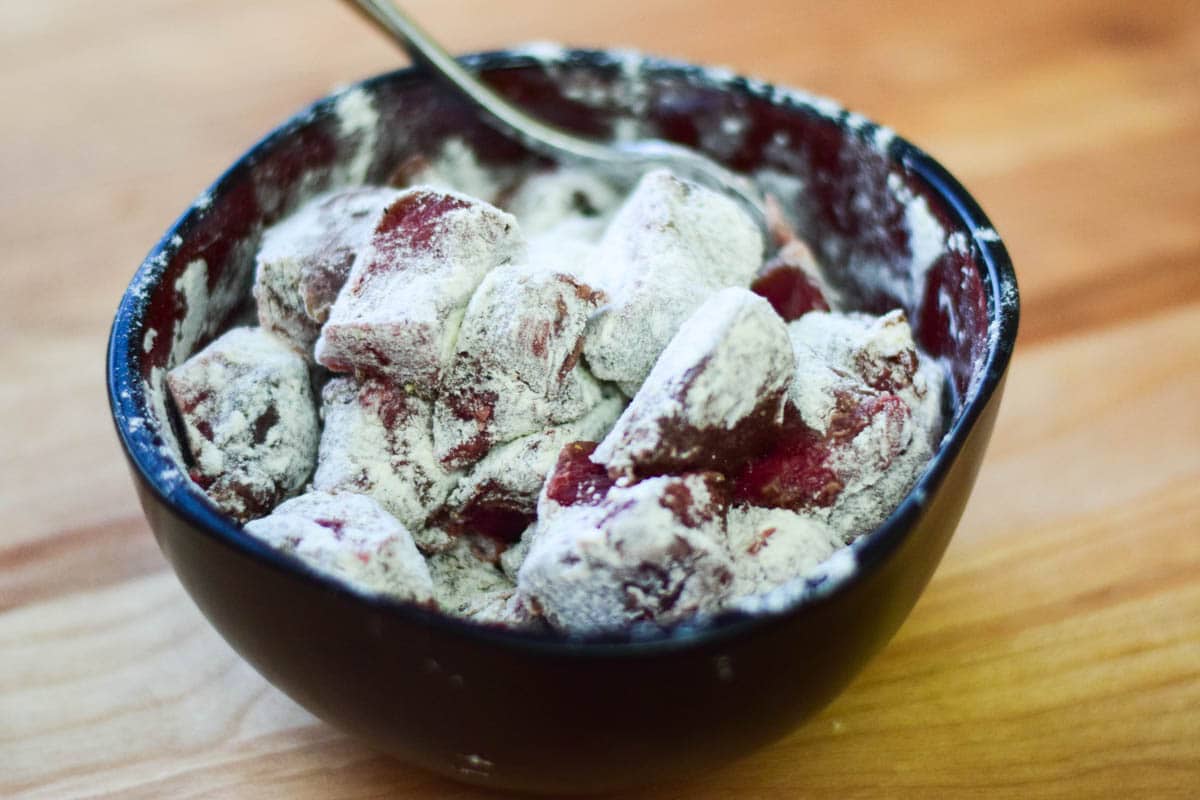 Deer meat cubes coated in flour in a mixing bowl.