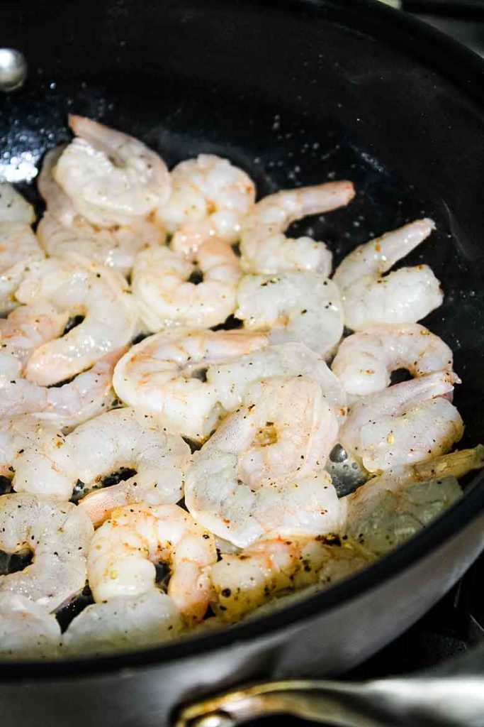 Raw shrimp in a hot skillet with butter.