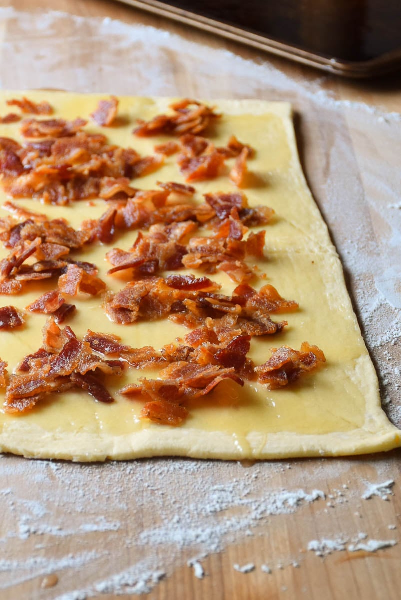 Roll dough spread with maple cream and bacon sprinkled before rolling up