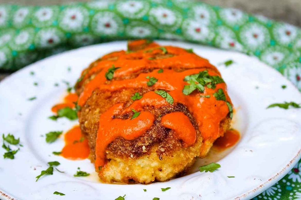 Fried chicken breast on a plate with red sauce drizzle.