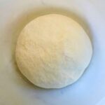 Homemade pizza dough ball in a mixing bowl.