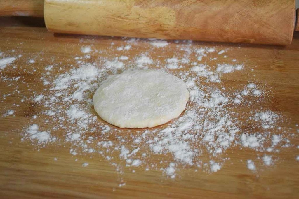 beginning to shape the dough into a tortilla on a floured board with a rolling pin