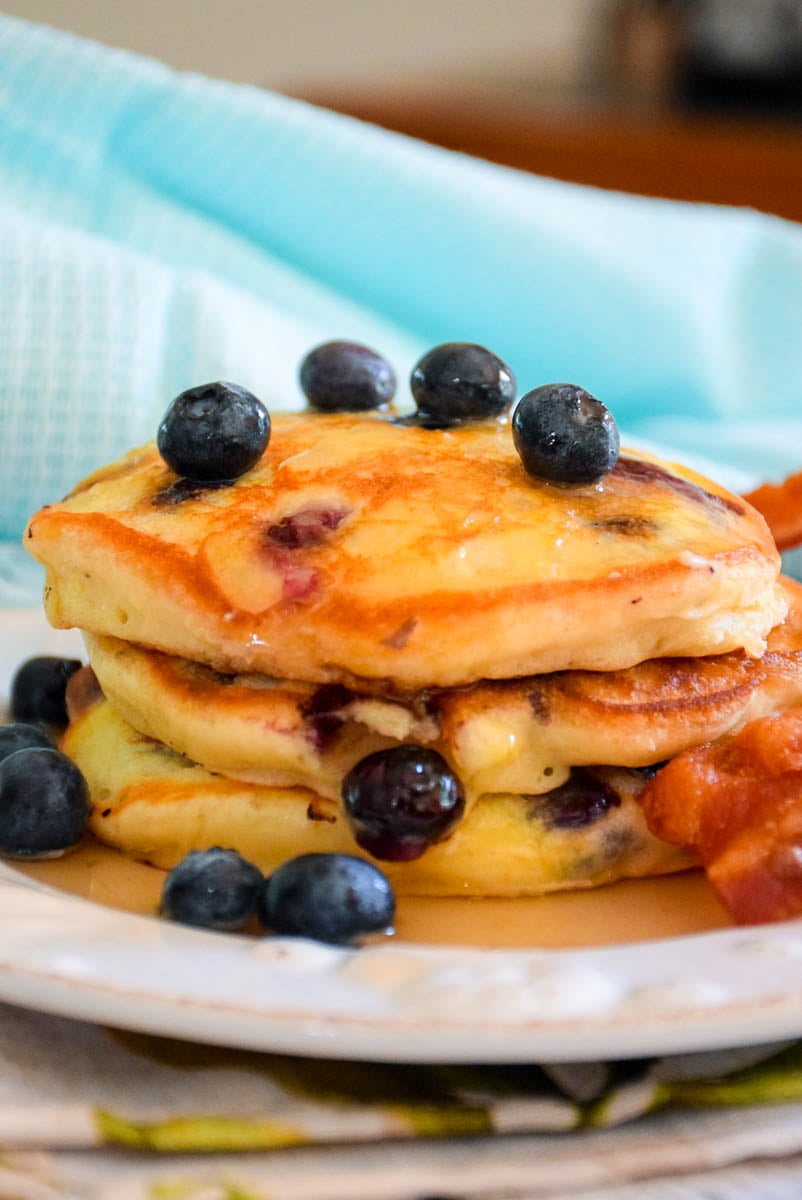 Stacked cakes topped with fruit and syrup and a side of bacon