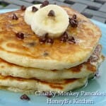 A stack of 3 chunky monkey pancakes on a blue plate garnished with banana slices and chocolate chips.