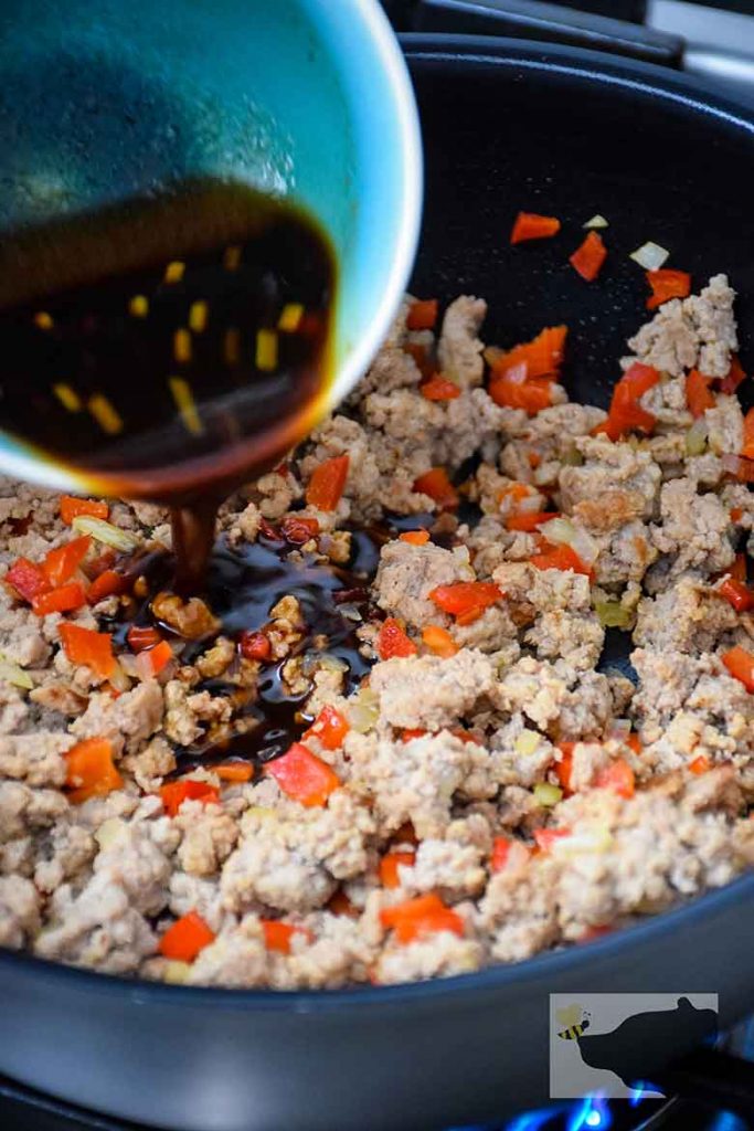 pouring sauce into skillet of browned ground turkey