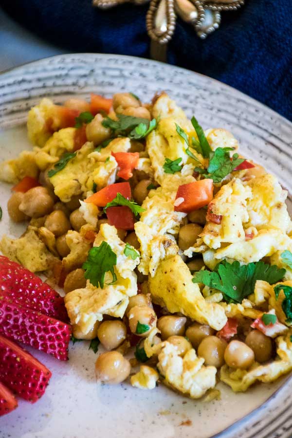 Overhead view of garlic scrambled eggs with chickpeas and cilantro with a large fresh strawberry to the left of the plate