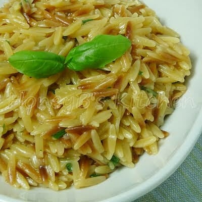 Upclose image of a white bowl full of cheesy orzo pasta and fresh basil garnish.