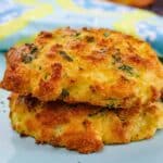 Close-up of two golden brown zucchini cheddar biscuits stacked on a light blue plate, showing crispy edges, melted cheese, and flecks of fresh herbs.