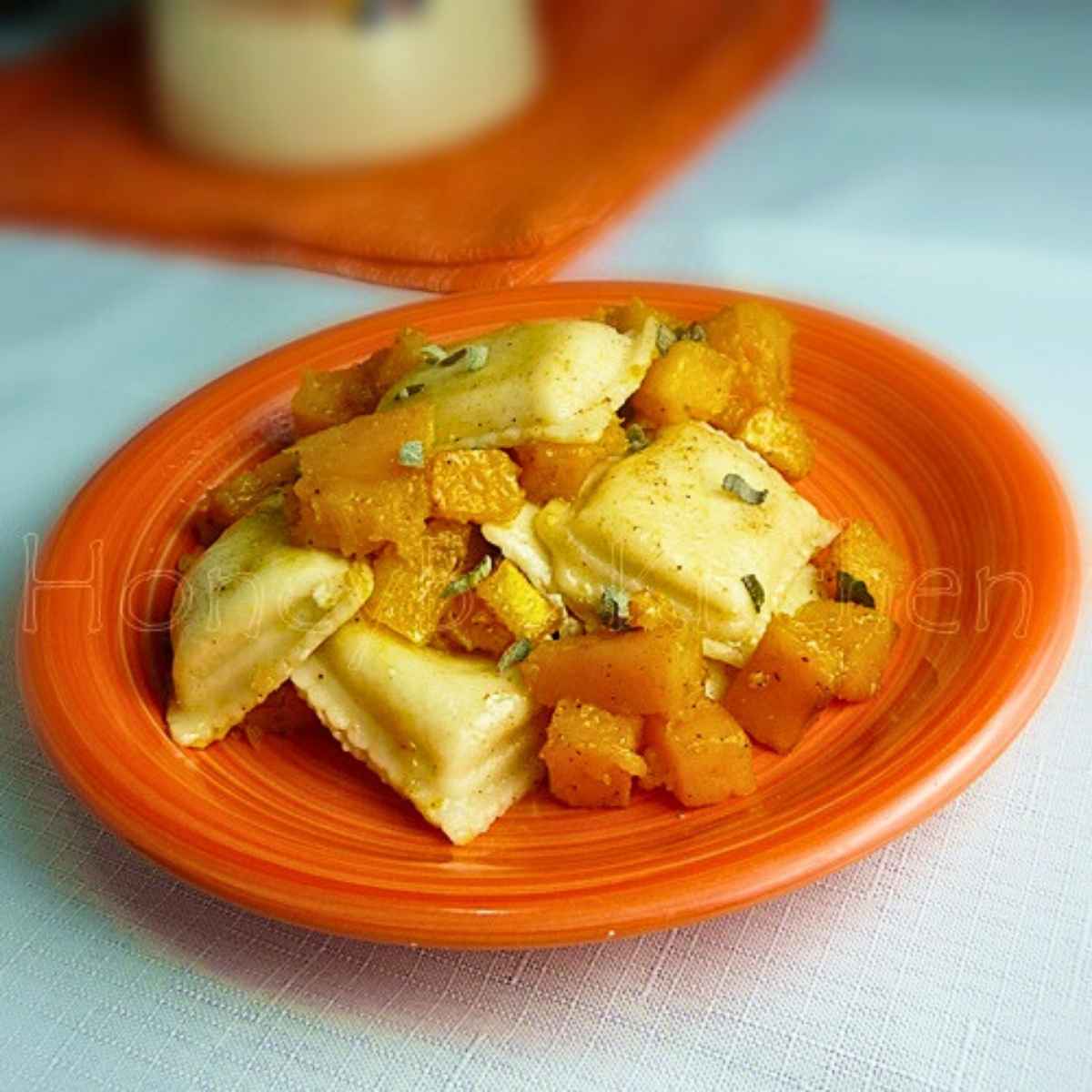 Cheese ravioli tossed with roasted butternut squash in a sage brown butter sauce served on an orange plate.