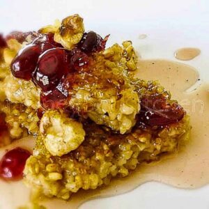 Sauteed steel cut oat cake topped with cranberry-infused maple syrup and toasted walnuts on a white plate.