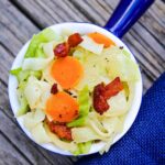 Overhead view of cabbage noodles with bacon, carrots, and onions in a white bowl with a blue handle.