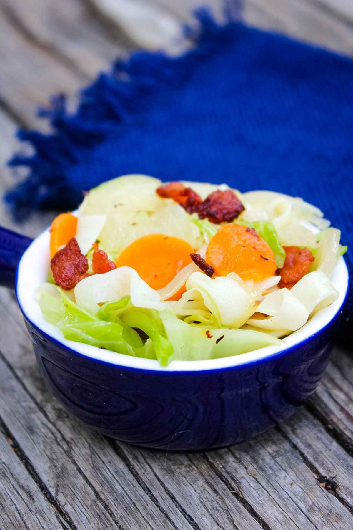 Cabbage Noodles with Bacon in a blue serving bowl with a blue napkin in the background.