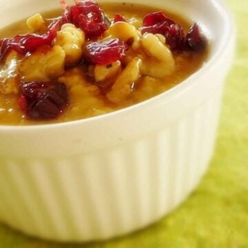 Pumpkin Steel Cut Oatmeal in a white bowl topped with dried cranberries and walnuts.