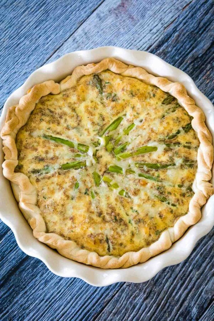 Overhead view of a whole baked tart with asparagus spears arranged around the circle.