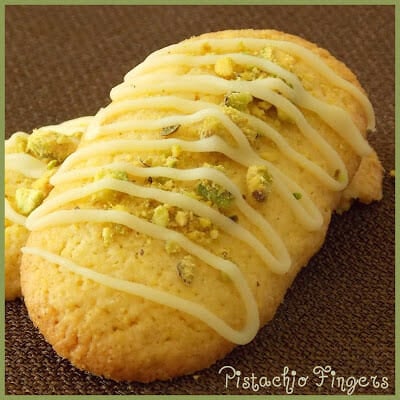Upclose image of two pistachio finger cookies drizzled with white icing and crushed pistachios.