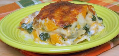 A slice of butternut squash lasagna served on a lime green plate, layered with golden roasted squash, spinach, onions, creamy cheese, and a browned cheesy topping.