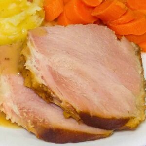 Two slices of bourbon glazed ham on a plate with a side of carrots and potatoes.