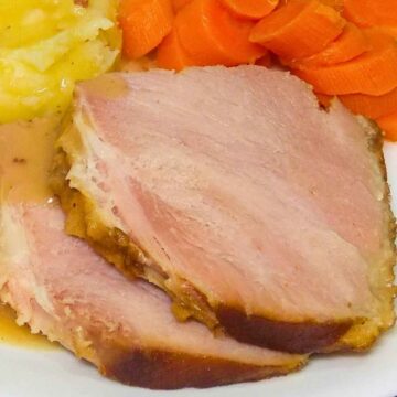 Two slices of bourbon glazed ham on a plate with a side of carrots and potatoes.