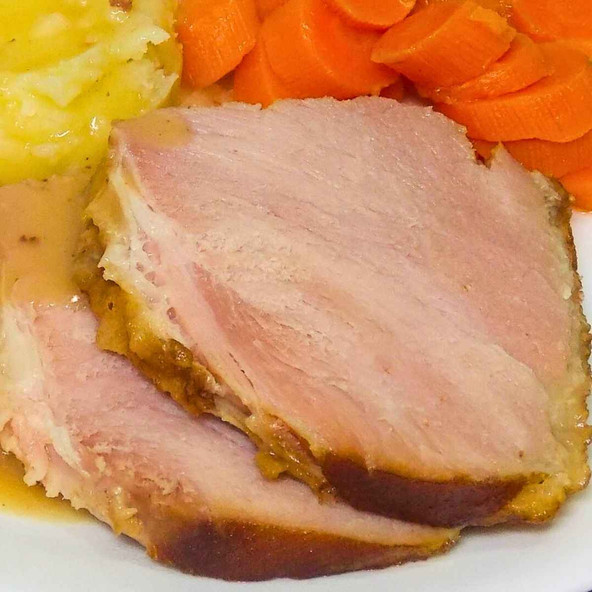 Two slices of bourbon glazed ham on a plate with a side of carrots and potatoes.