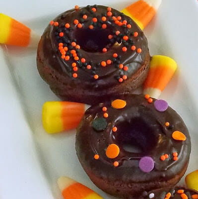 Two mini chocolate pumpkin donuts on a white plate.