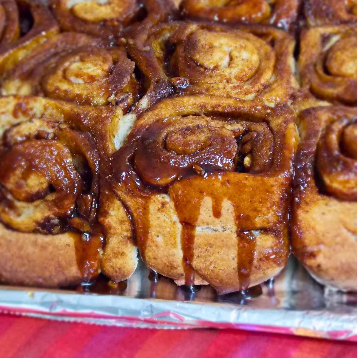 Freshly baked sticky buns in a pan topped with a glossy caramel glaze dripping down the swirls.