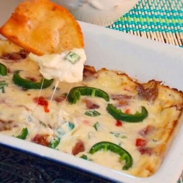 Baked Jalapeno Popper Dip with a tortilla hovering over the dish and dip on the chip.
