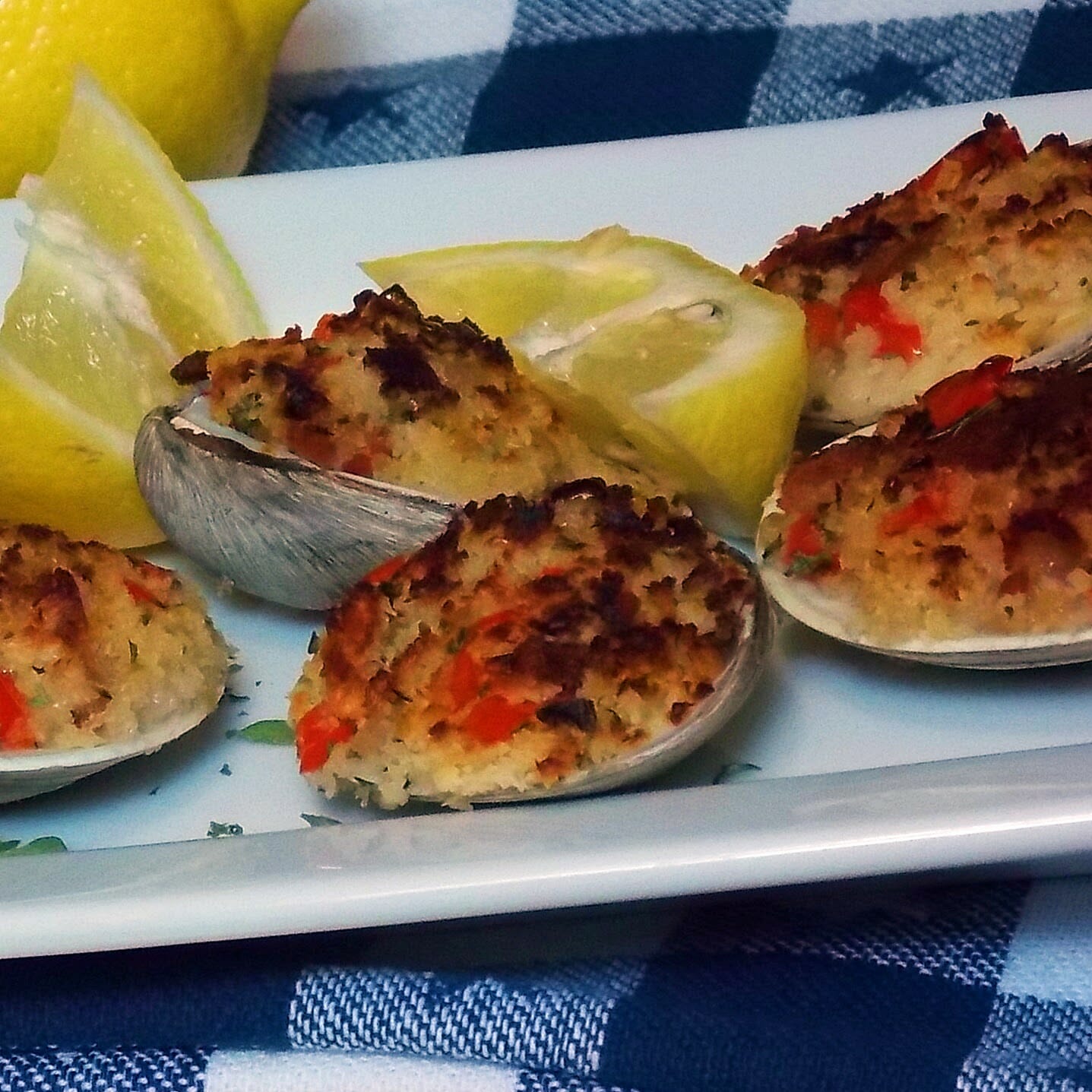 Seasoned breadcrumb stuffed clams with pancetta on a white serving tray with lemon wedges.