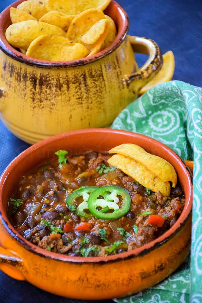 Black Bean Chili in an orange bowl topped with jalapeno and corn chips