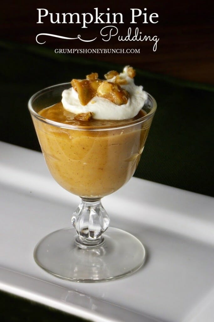 An image of pumpkin pie pudding in a clear glass footed dessert dish topped with a tablespoon of whipped cream and peanut brittle.