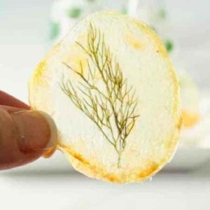 Close up image of a window pane potato chip with fresh dill in the center of the chip.