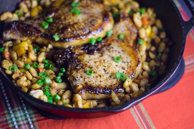 Glazed pork chops in a cast iron skillet on top of white beans sprinkled with green onions