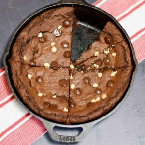Nutella Chocolate Brownies baked in a cast iron skillet, topped with white and dark chocolate chips, with one slice removed to show the fudgy center.