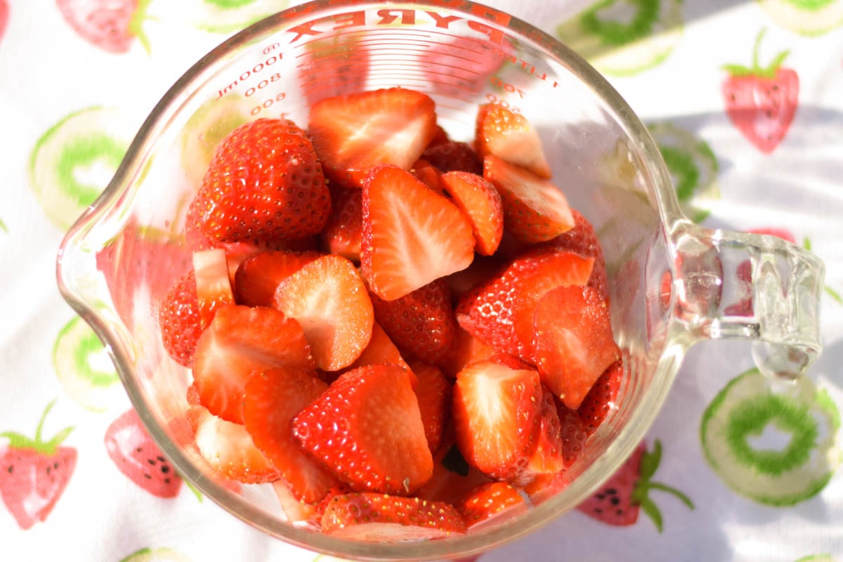 Sliced strawberries in a glass measuring cup.