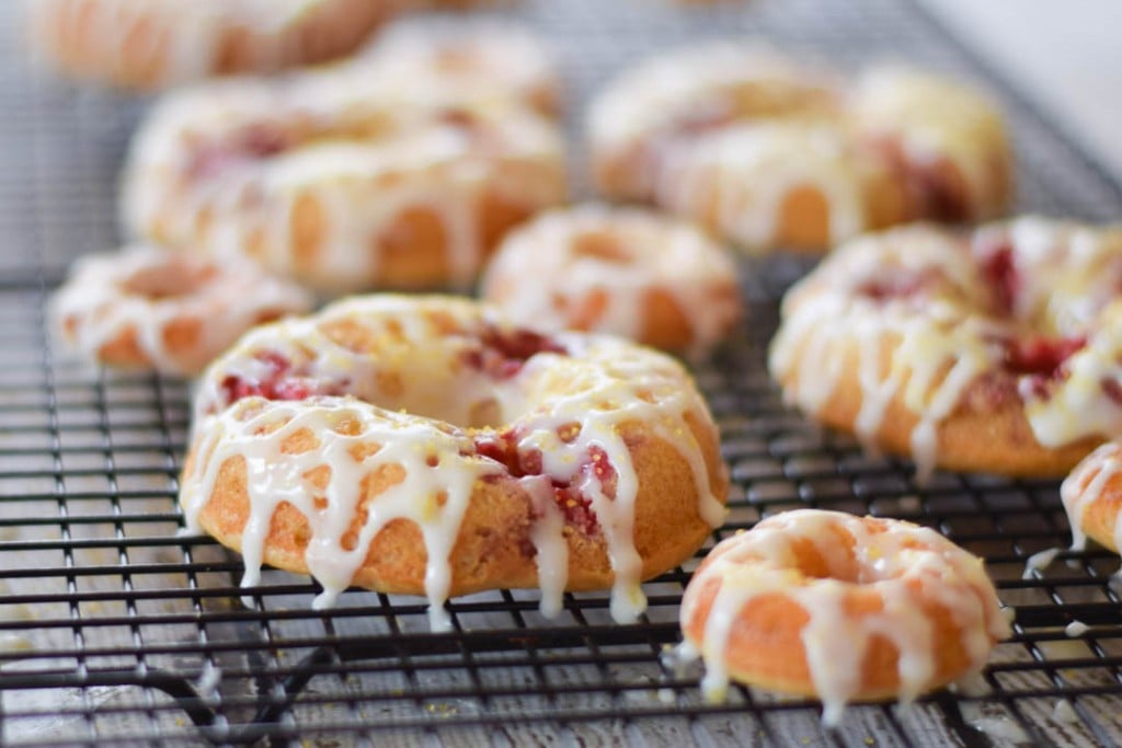 Raspberry Baked Lemon Donuts on a cooling rack with the icing drizzled over top.