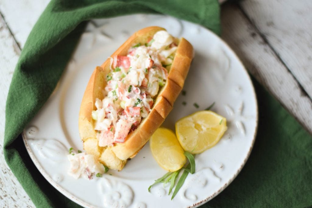 Overhead view of Classic Lobster Rolls on a seashell plate with lemon wedges and a green napkin