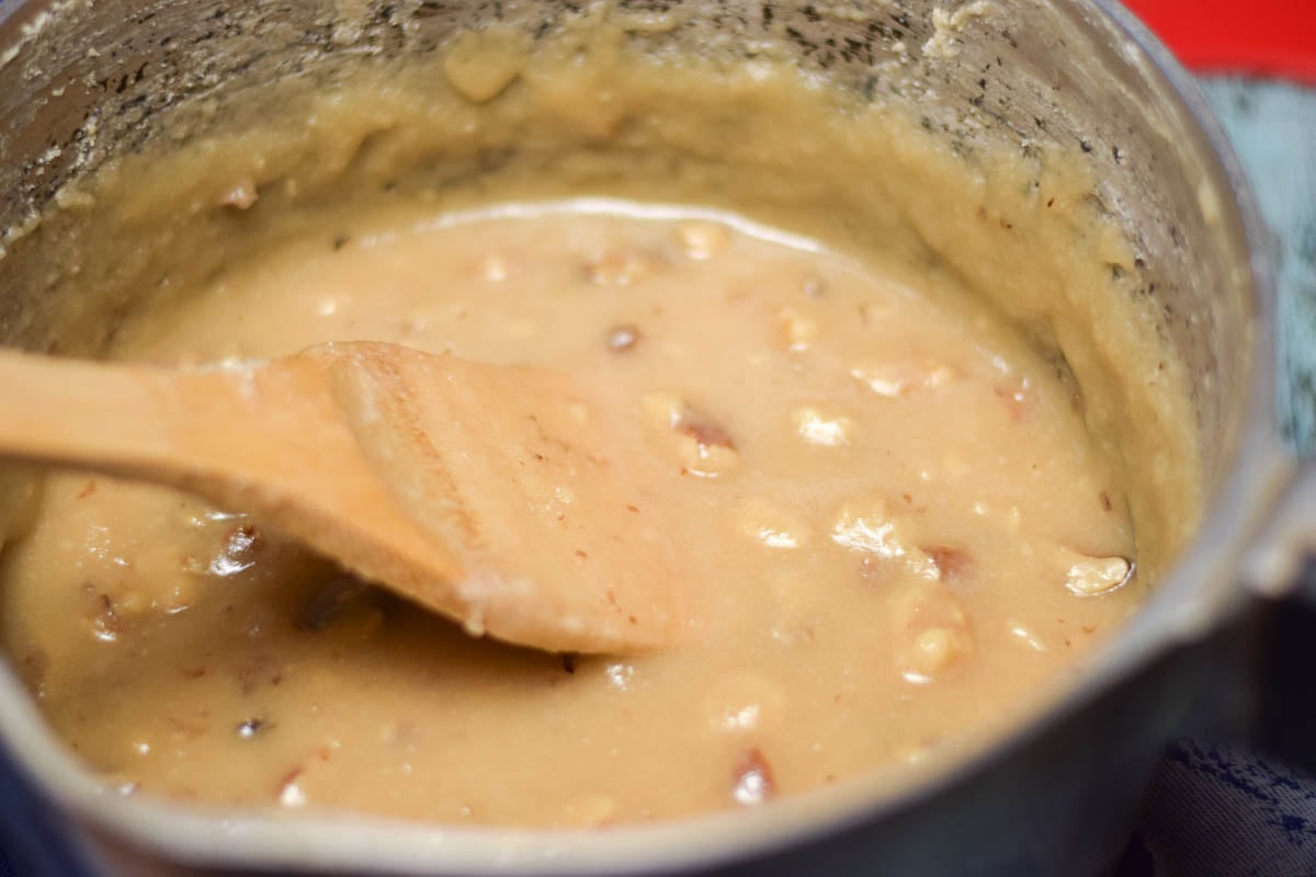 Maple walnut fudge in saucepan being stirred with a wooden spoon.