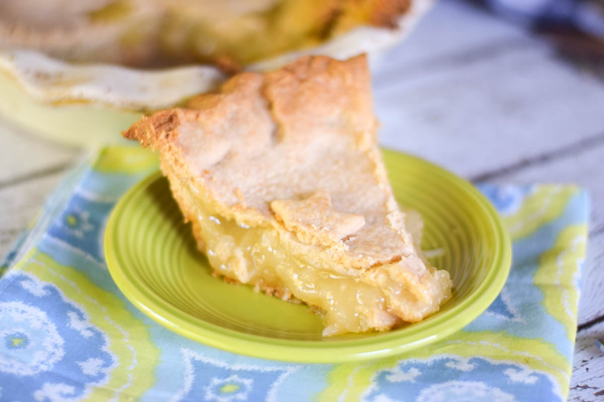 A slice of pineapple pie on a neon green plate with the whole pie dish in the background