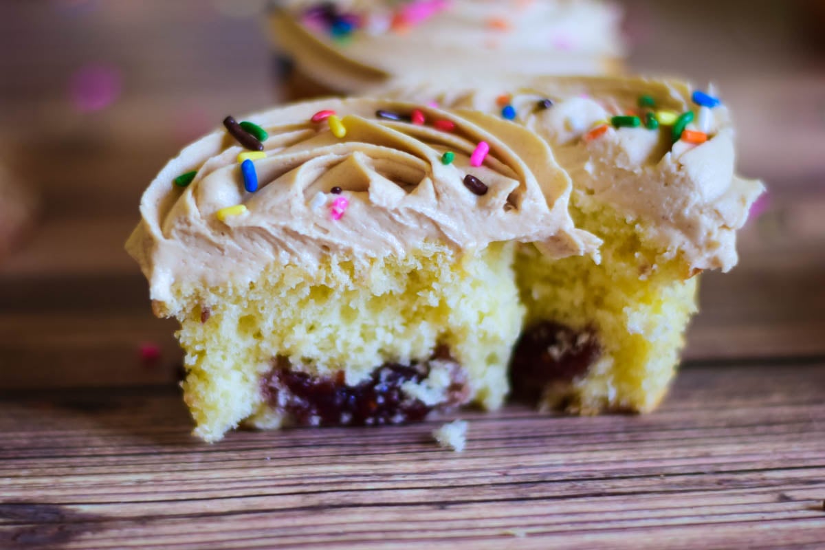 A vanilla cupcake with jam filling and peanut butter frosting cut in half to show the inside of the cupcake.