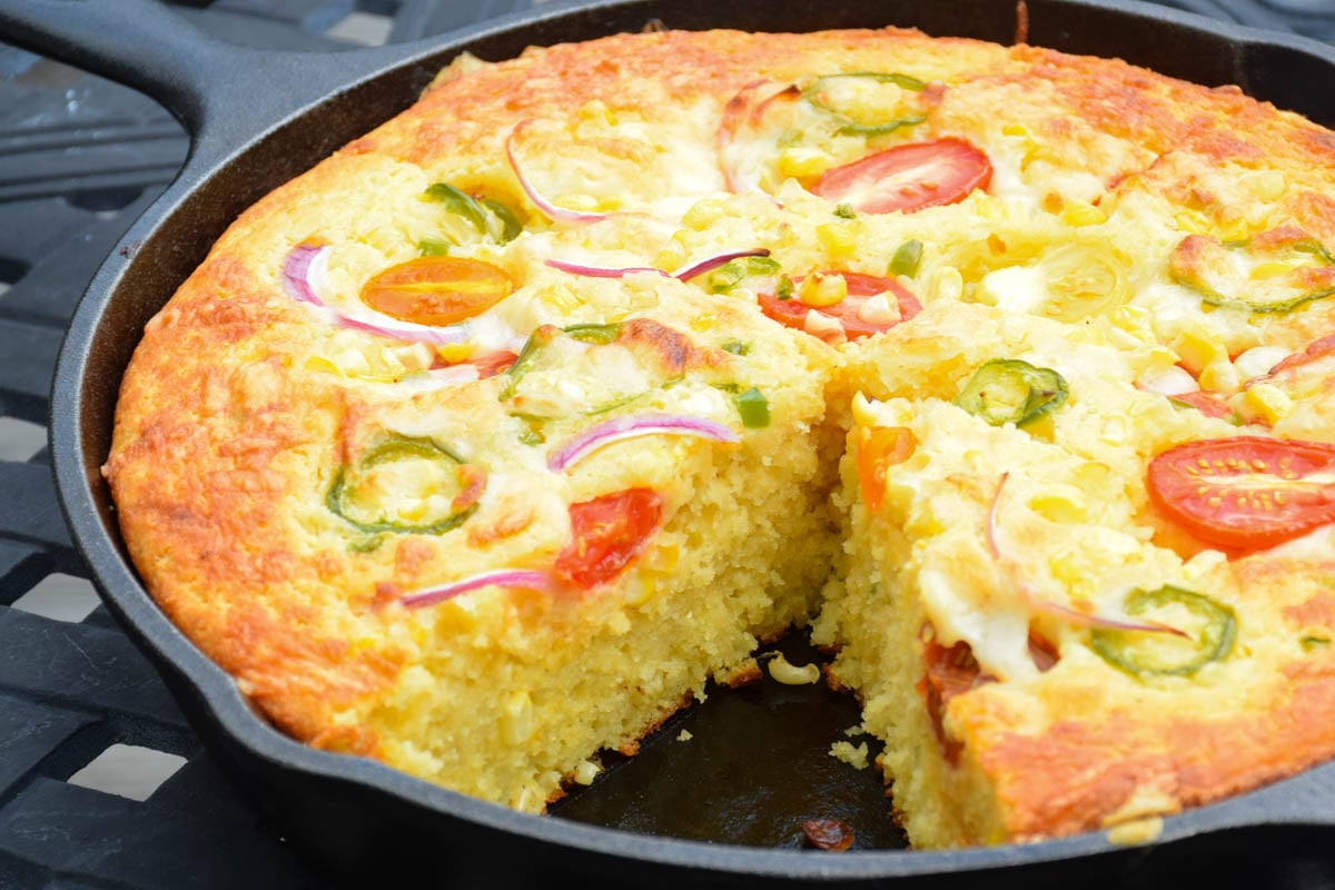 Baked Cheesy Jalapeno Cornbread in a cast iron skillet with one slice removed.