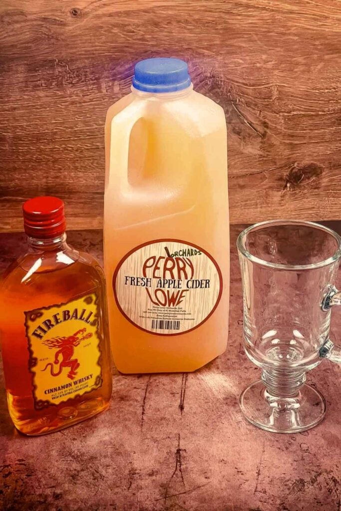 A bottle of Fireball Whisky, just of fresh apple cider, and an empty glass mug.